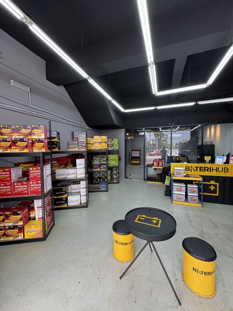 Interior of a Baterihub retail store displaying various car battery brands and a customer service counter.