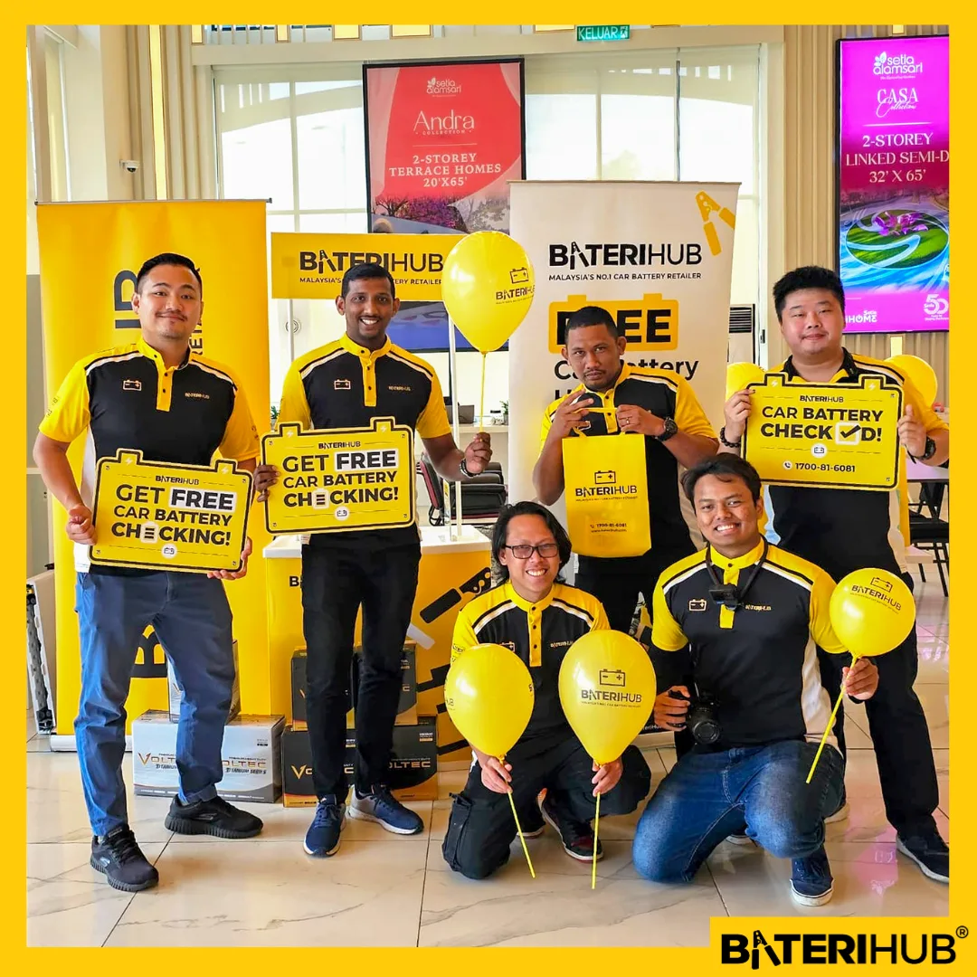 BateriHub team promoting free car battery health check event with branded signage and balloons at indoor corporate event in Malaysia.
