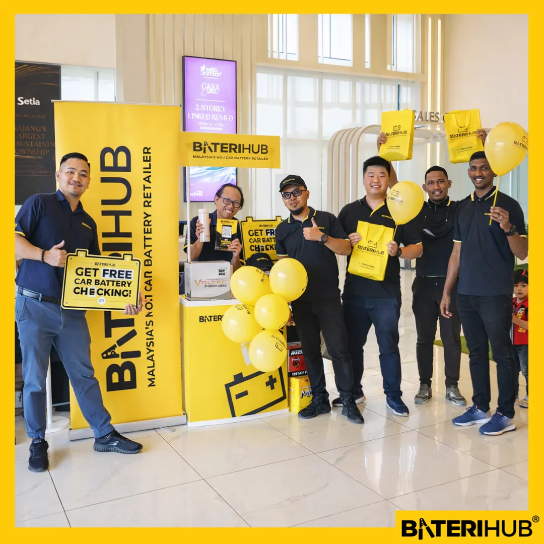BateriHub team promoting free car battery checking at a mall booth with yellow branding, balloons, and promotional bags.