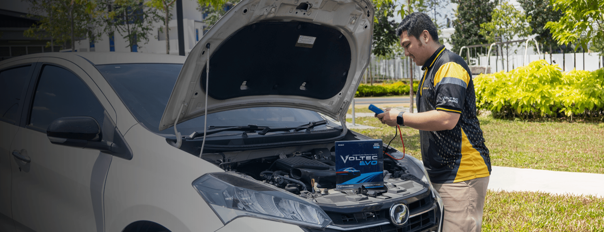 BateriHub technician testing a car battery under the hood using diagnostic equipment with a Voltec Evo battery placed on the engine bay.